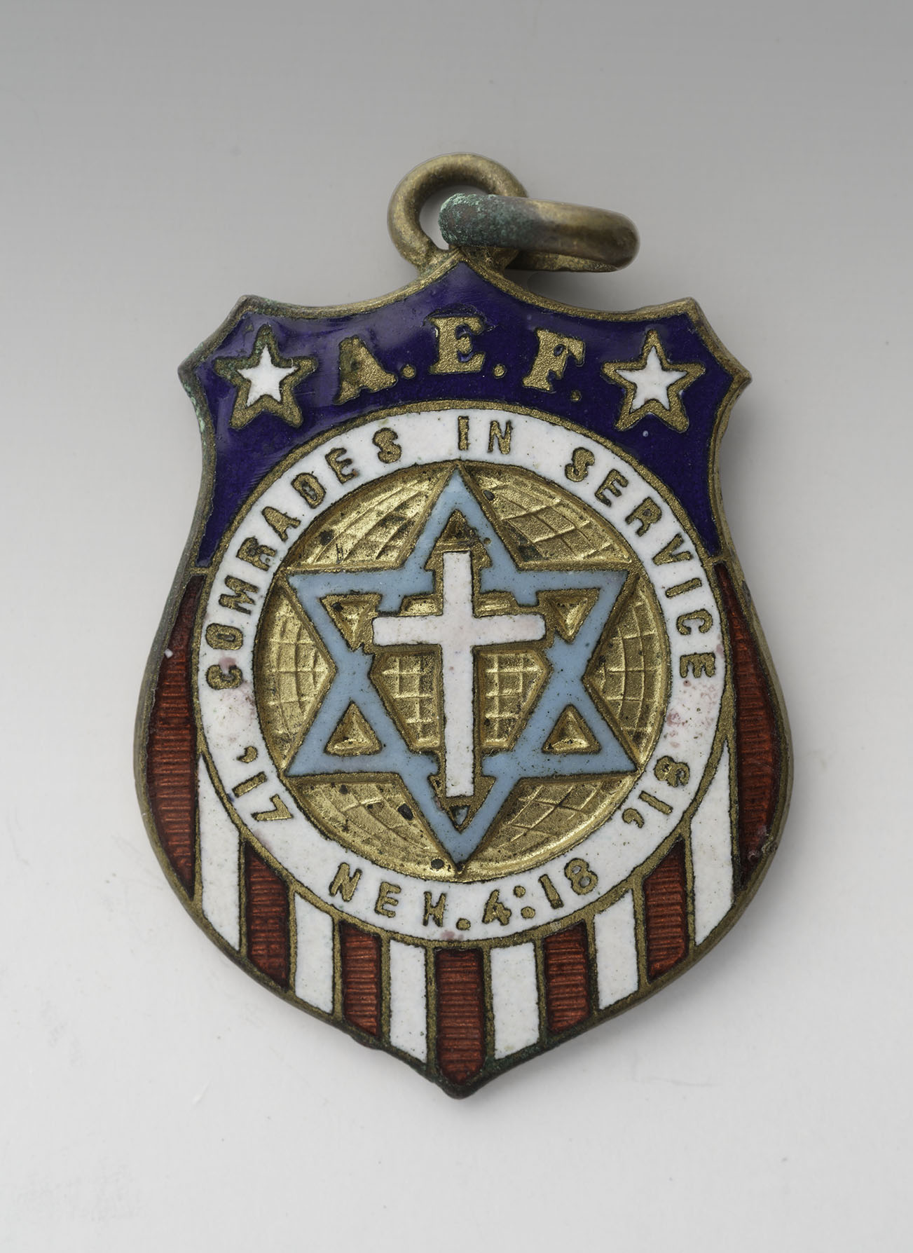 Modern photograph of a small charm shaped like a shield in the colors of the U.S. flag. In the center a cross is inside a star of David. Text engraved around the cross and star: "Comrades in Service / '17 '18 /  Neh. 4:18"