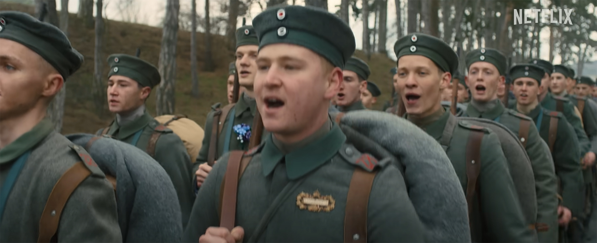Film still of two lines of WWI soldiers in German uniform marching along while singing