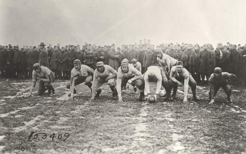 Photographie en noir et blanc d'une ligne de mêlée lors d'un match de football nord-américain.