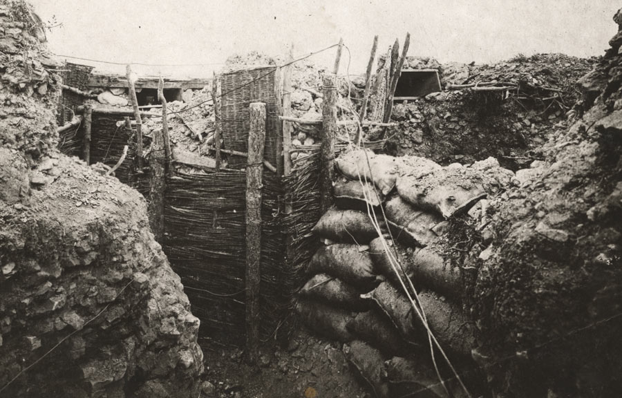 Black and white photograph of the inside of a trench lined with sandbags and wooden stakes.