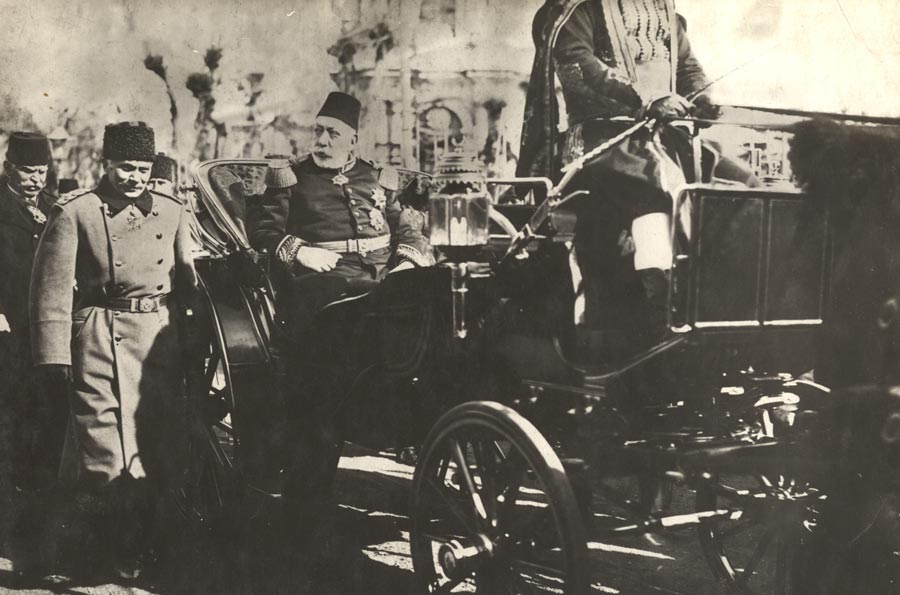 Photographie en noir et blanc d'une calèche étincelante transportant un vieil homme barbu corpulent portant un fez et un uniforme militaire décoré.