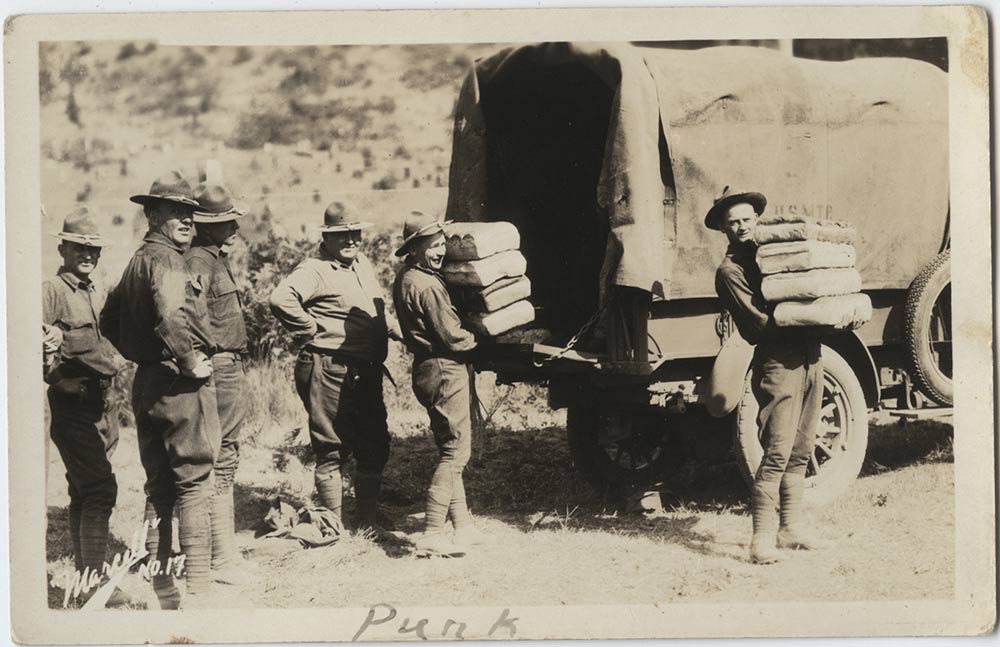 Black and White photograph of American WWI soldiers in uniform unloading stacks of bread loaves from the back of a truck