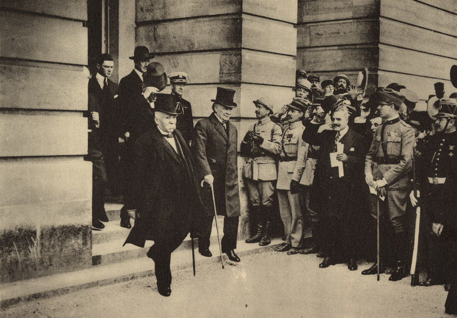Sepia photograph of several older white men in top hats and overcoats descending a short set of stairs into a courtyard filled with a crowd of soldiers and onlookers.
