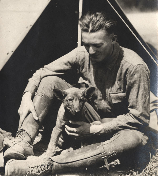 Black and white photograph of a seated white man in military combat uniform with a small dog in his lap.