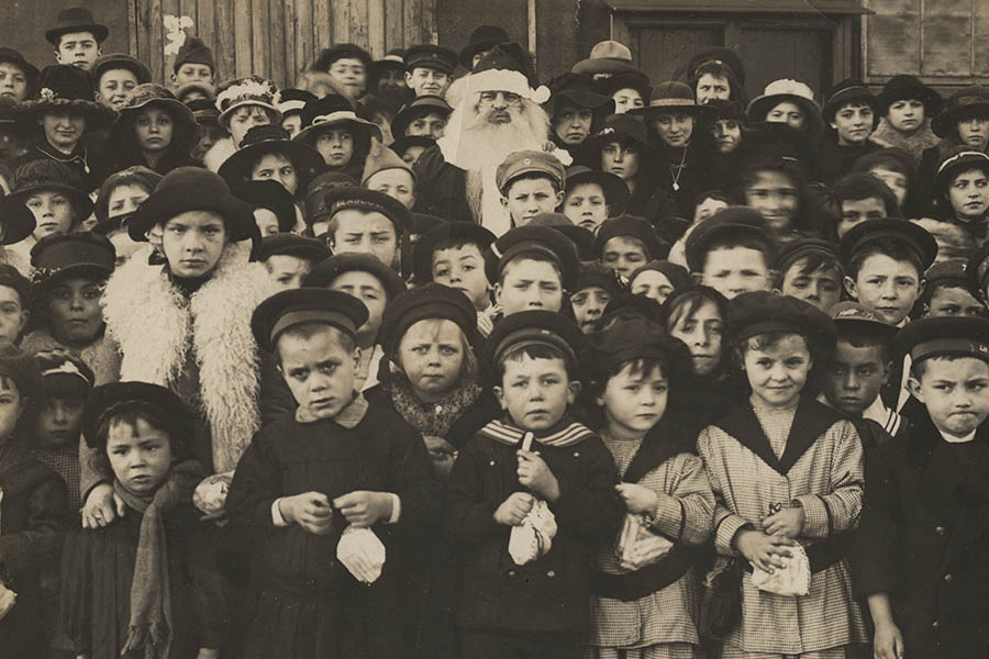 Photographie en noir et blanc d'une grande foule d'enfants avec un homme déguisé en Père Noël au milieu.