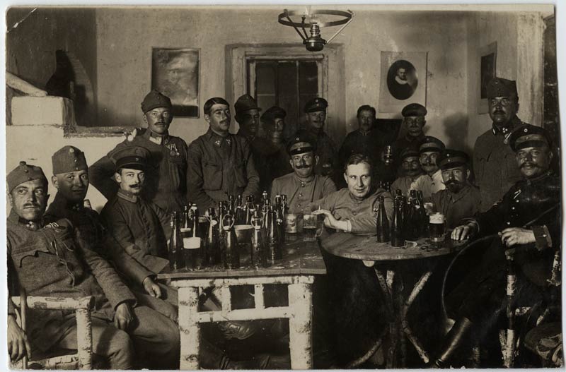 Large group of soldiers gathered around two tables covered in beer bottles.