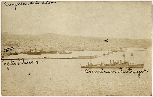 Sepia photograph of a harbor with multiple battleships in it. Two of them are labeled 'American Destroyer' and 'English Cruiser' in cursive.