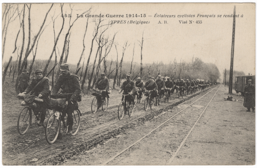 Black and white photograph of a double line of men in military uniform riding bicycles towards the viewer's left.
