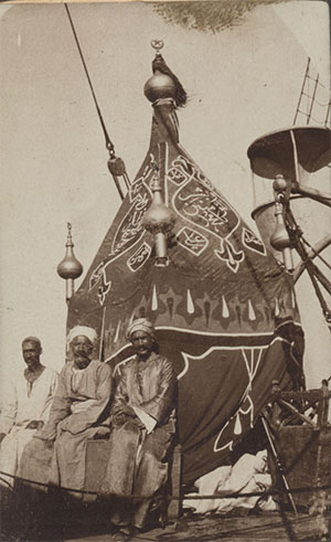 Three Arab or Egyptian men sitting outside a tent-like structure with ornate designs on the outside walls.