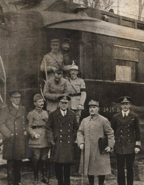 Sepia photograph of nine men arrayed on and in front of a train car all in military uniform and winter coats.