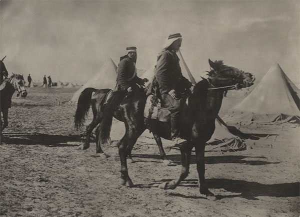 Black and white photograph of two WWI-era men dressed in Turkish soldier uniforms riding on horses