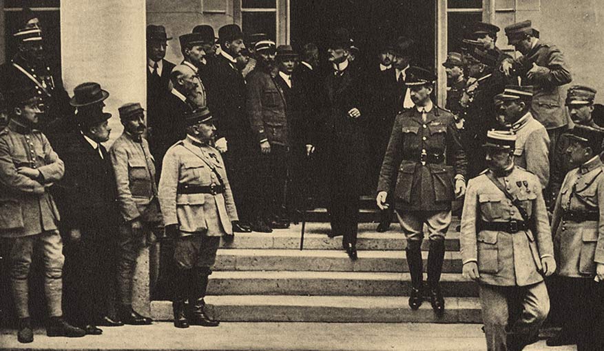 Sepia photograph. A small group of white men in civilian top hats and suits exit a large doorway and go down a short flight of stairs into a courtyard. They are surrounded by soldiers and onlookers.