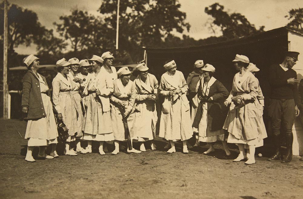 Sepia photograph of a group of white women wearing dresses and baseball caps laughing together.