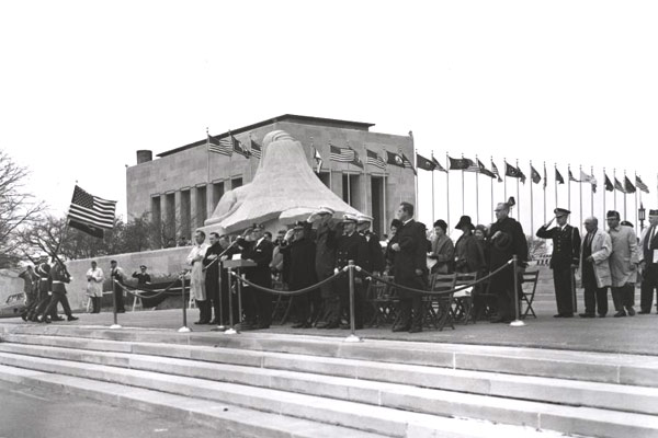 Black and white photograph of the "Memory" sphinx and Exhibit Hall surrounded by people and flags.