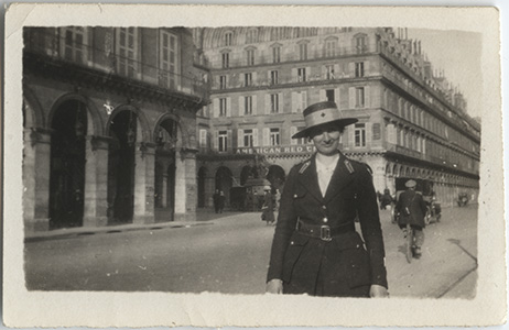 Black and white photo of a woman in a walking suit and hat standing in a European city street.