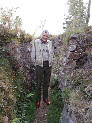 Modern photograph of a man in a canvas jacket standing in a grassy trench.
