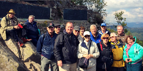 Photograph of a group of tourists standing next to or perched on a rocky outcrop overlooking a green valley.