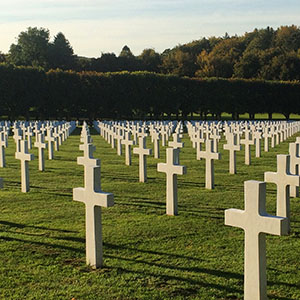 Modern photograph of many rows of white crosses in a green field.
