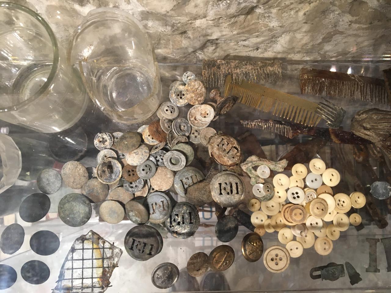 Antique buttons, coins, glass cups and combs in a museum display.
