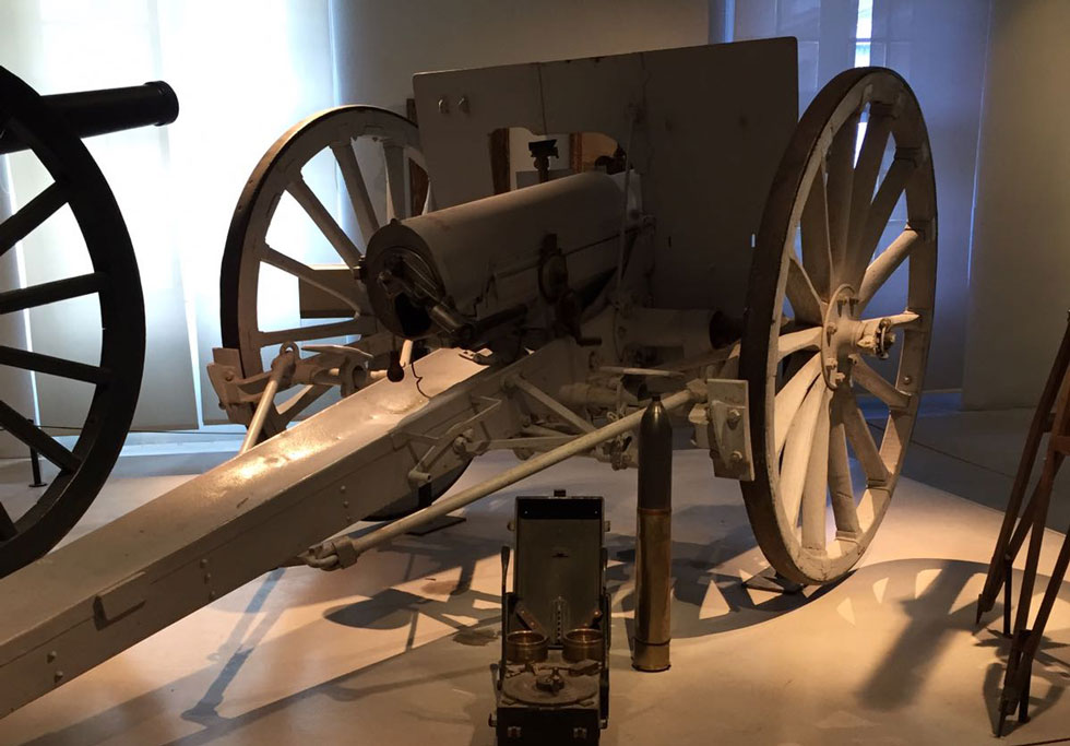 Photograph of a museum display of a trench gun on large wheels.