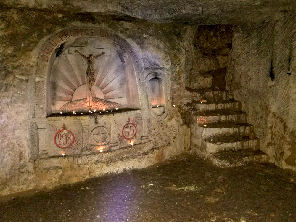 Photograph of an underground cave-like area. An altar with a crucifix is carved into the wall.