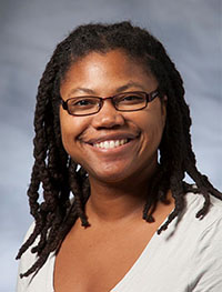 Headshot of a Black woman with glasses and braided hair wearing a white shirt