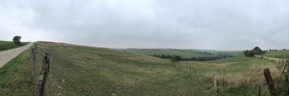 Panorama of a wide grassy field under a cloudy sky.