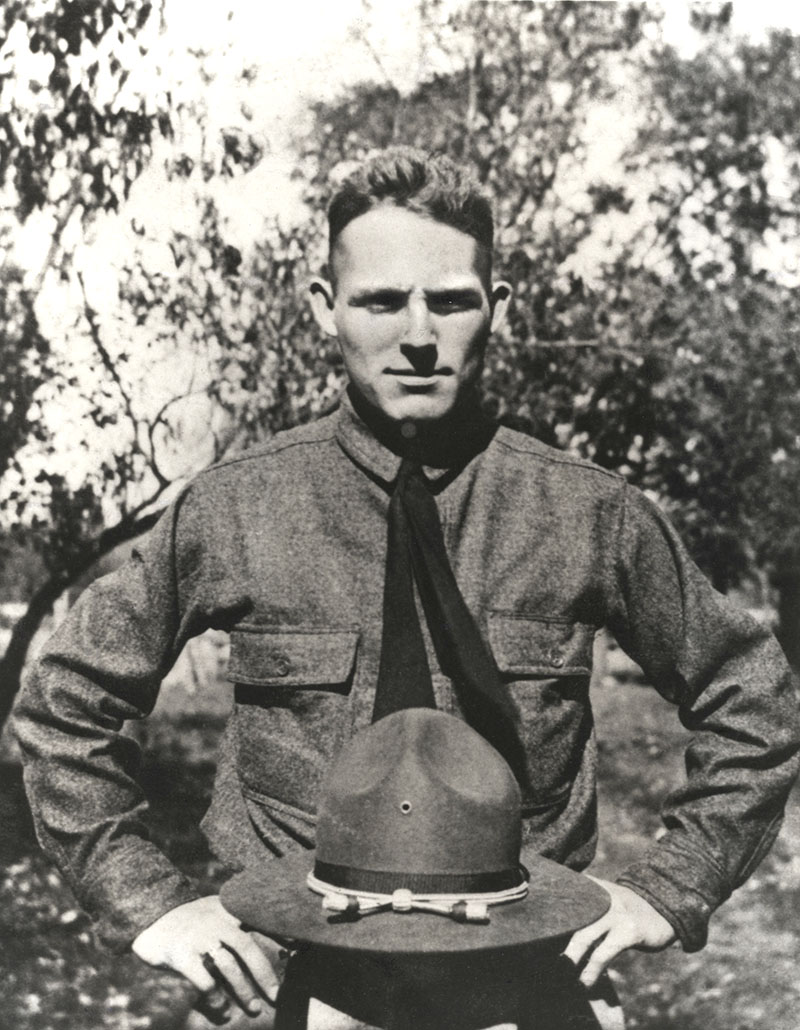 Portrait of a young white man in military uniform with his wide-brimmed hat resting on a post in front of him