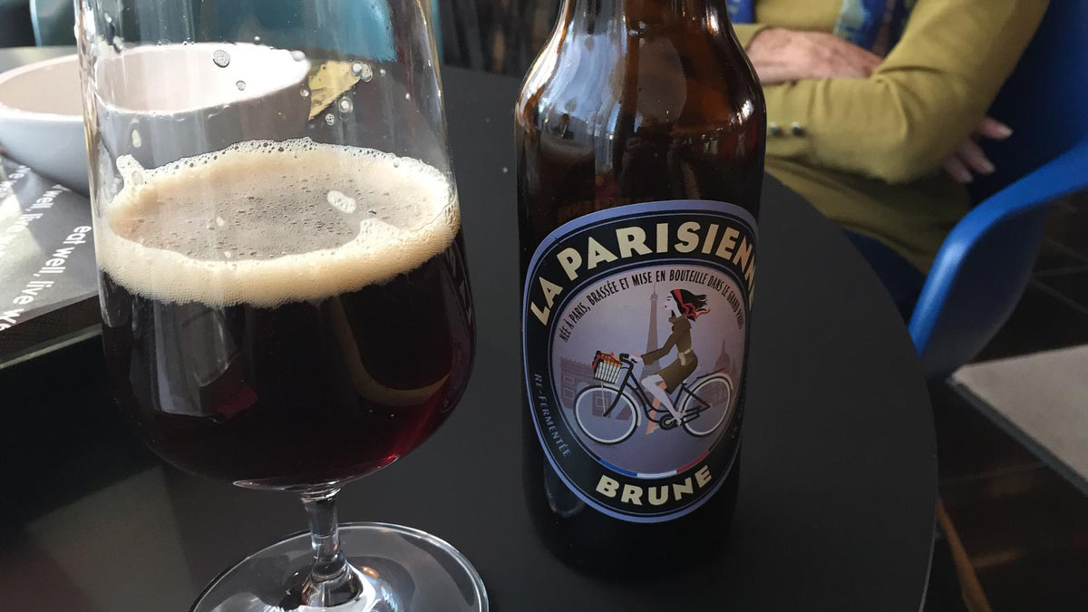 'La Parisienne Brune' beer bottle next to a stemmed beer glass