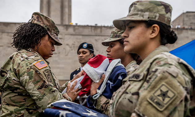 Modern photograph of a soldier giving a US flag to another soldier while a third soldier stands ready with a folded flag.