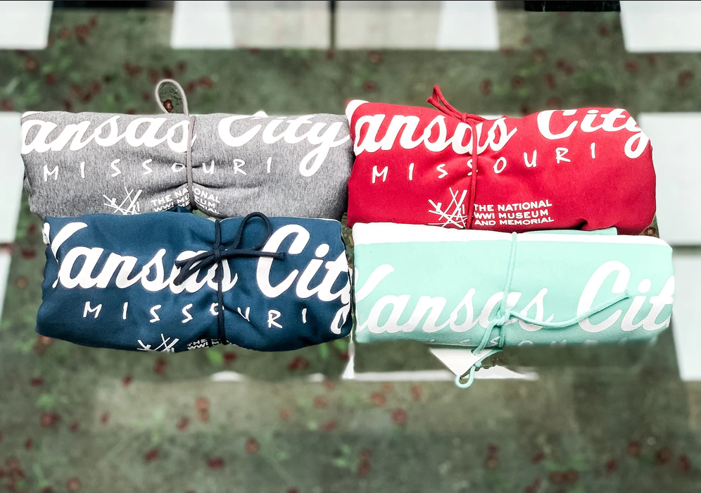 Four rolled-up blankets of different colors, printed with the words 'Kansas City' in cursive font