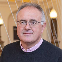 Headshot of a white man with grey hair wearing glasses and a dark grey sweater