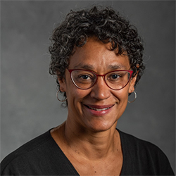 Headshot of a Black woman with short curly hair wearing red glasses and a black shirt