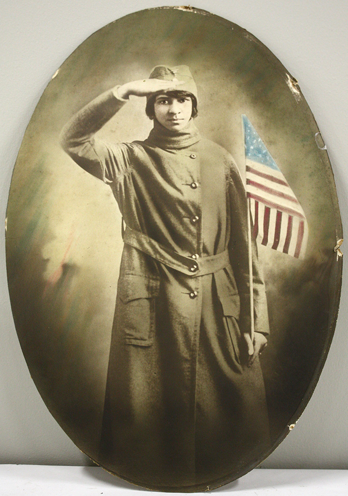 Sepia photograph in an oval frame of a young Black woman wearing a cap and trenchcoat uniform, saluting and holding a U.S. flag.