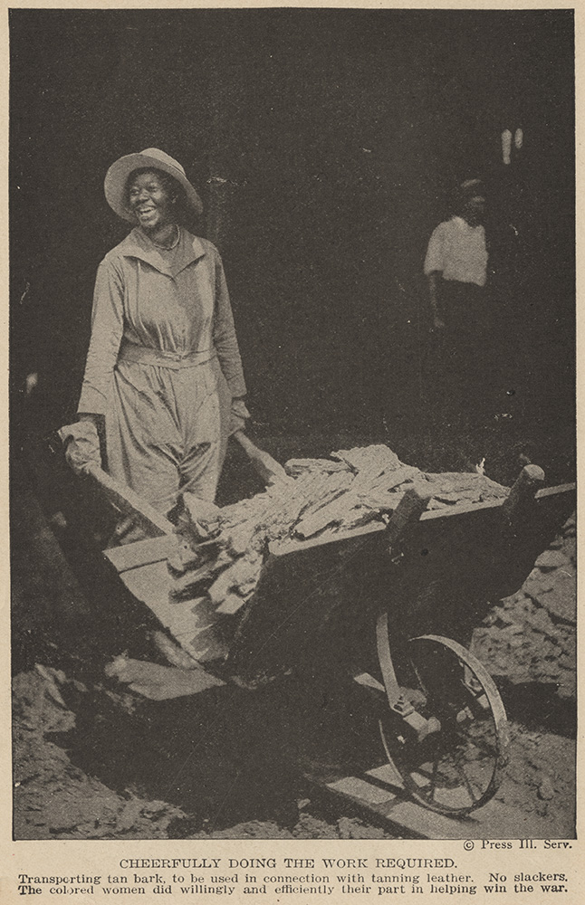 Black and white photograph of a Black woman dressed in coveralls and a wide-brimmed hat pushing a loaded wheelbarrow. She is smiling and looking off to the side.