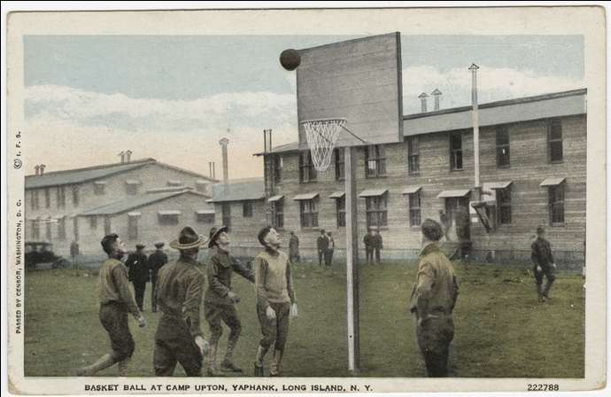 Photographie colorisée de jeunes hommes blancs en uniforme militaire jouant au basket-ball sur un terrain herbeux entre les casernes.