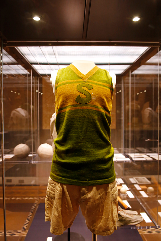 Modern photograph of a green and yellow basketball uniform in a glass display case.