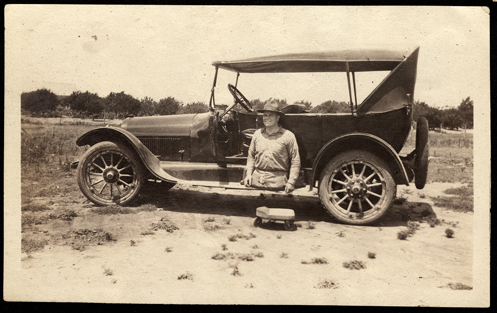 Black and white photograph of a wounded soldier sitting on the edge of car. The soldier has lost both of his legs.