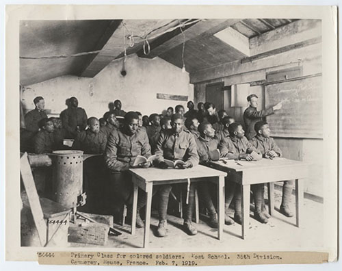 Black and white photograph of a classroom full of Black soldiers sitting two to a desk.