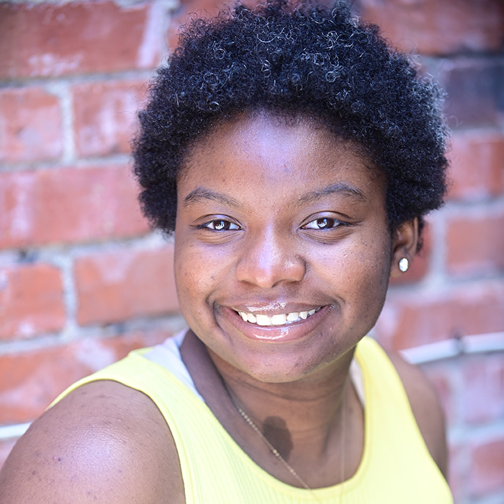 Modern headshot of a young Black woman with a short curly afro, smiling at the viewer.
