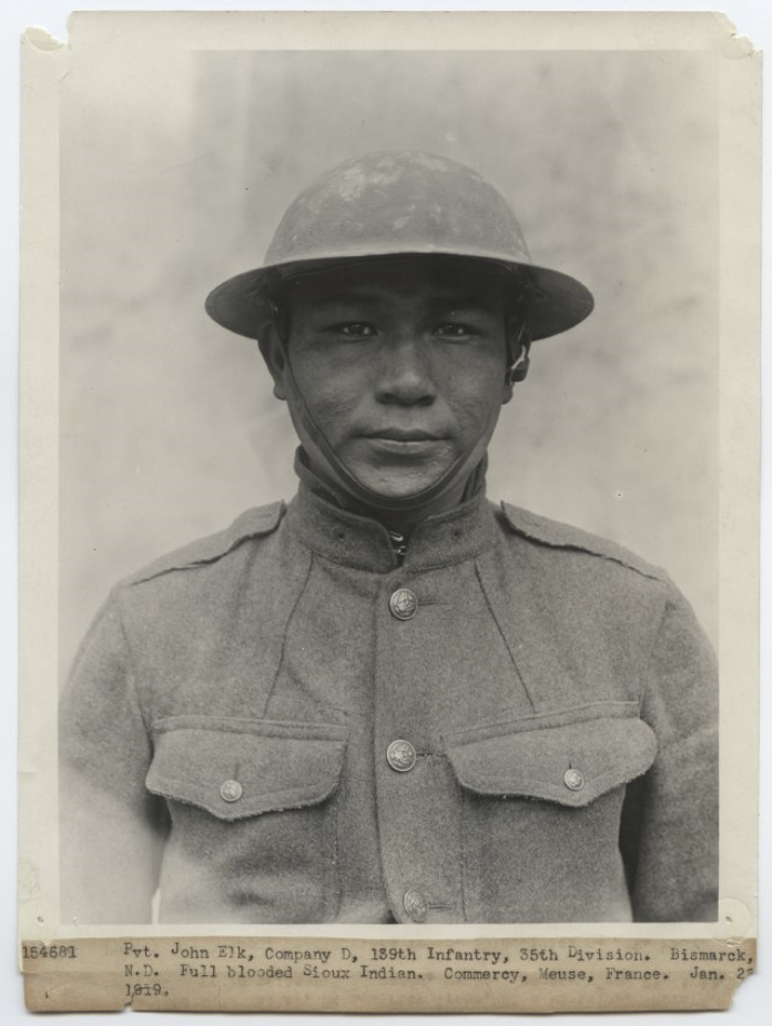 Photographie portrait en noir et blanc d'un jeune amérindien en uniforme militaire américain de la Première Guerre mondiale et casque de pâte en métal.