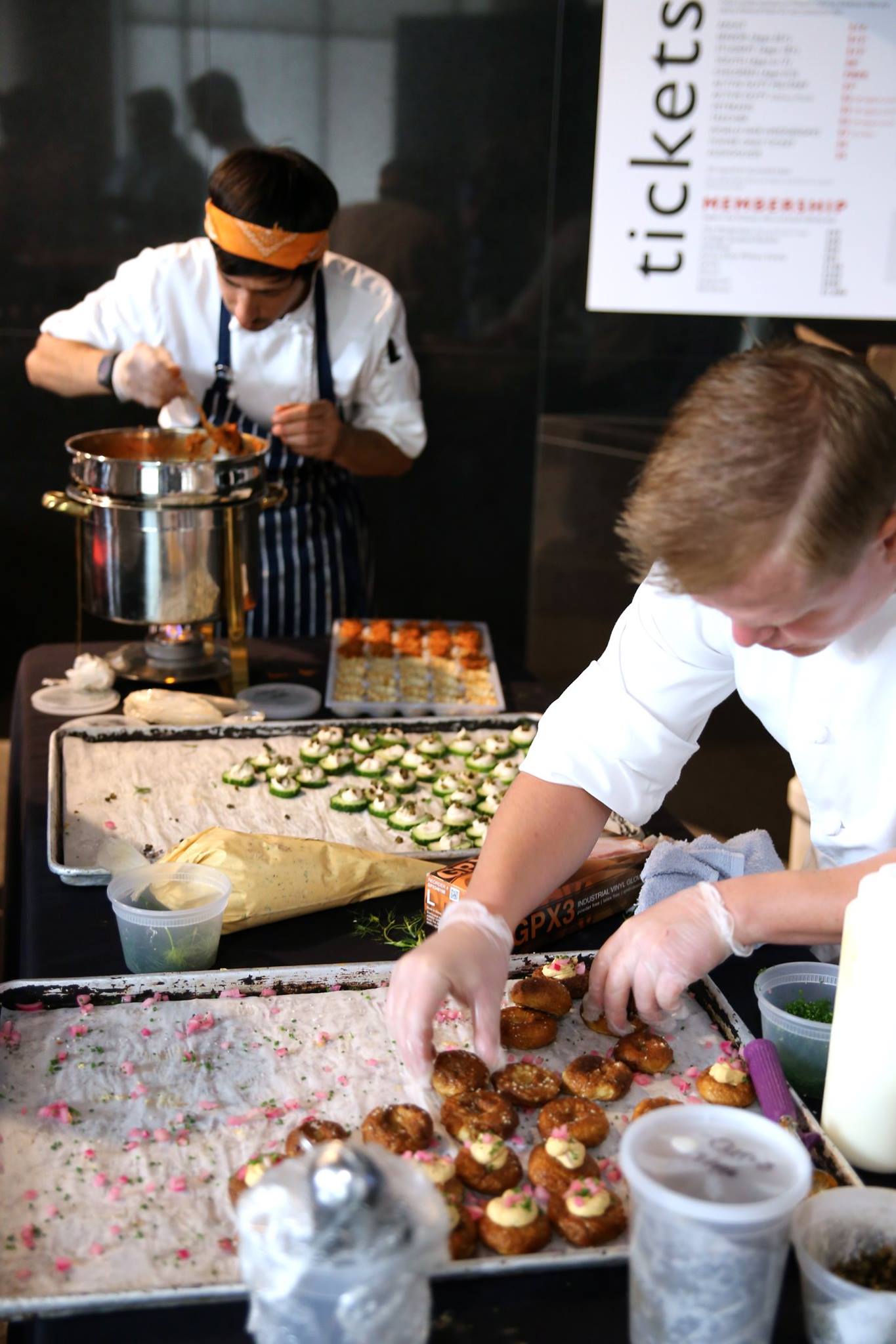 Modern photograph of two young white chefs cooking and plating trays of hors d'oeuvres in the Museum and Memorial's main corridor.