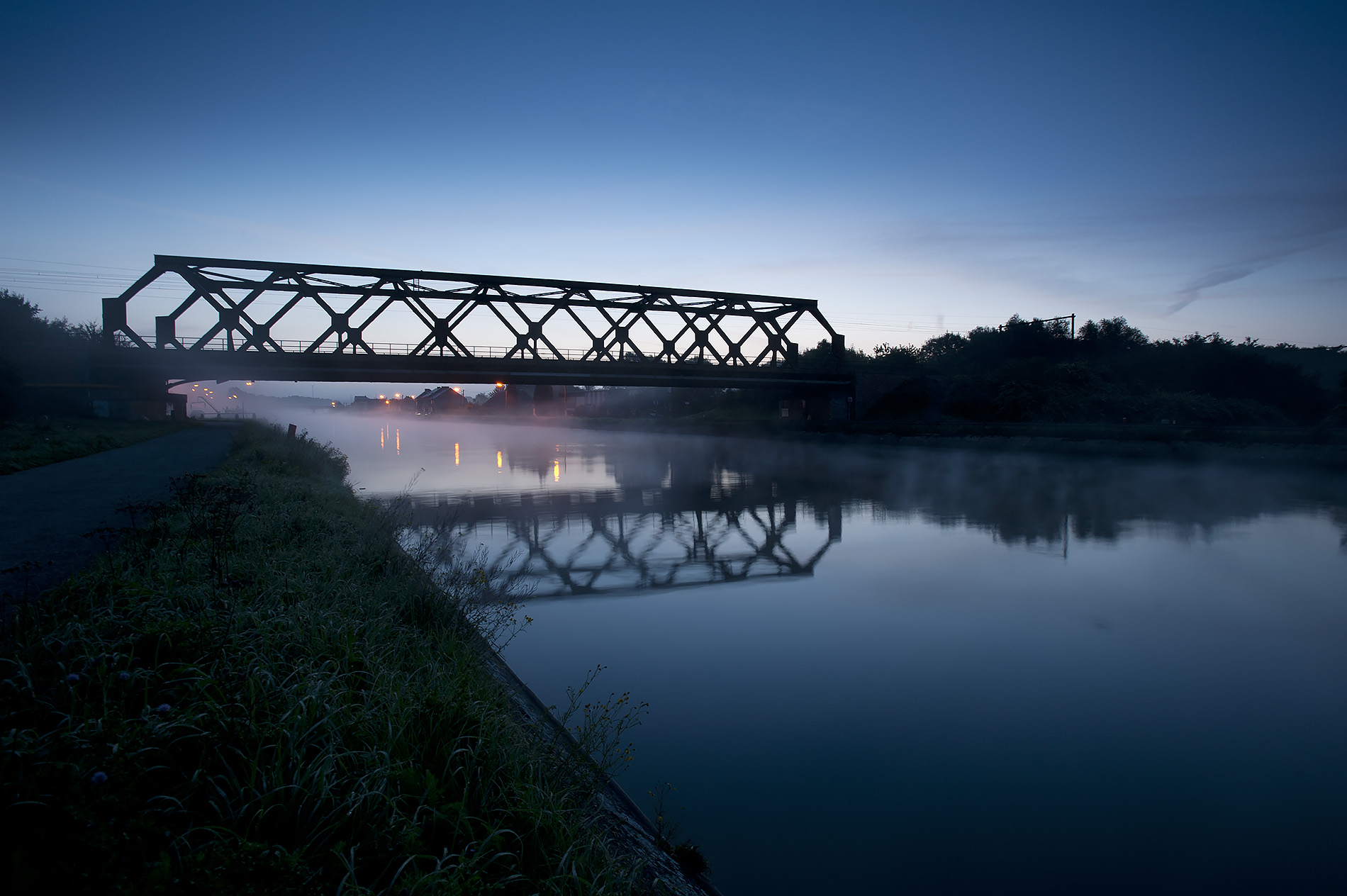 Modern photograph of a bridge across a river at dusk, with forest on both banks.