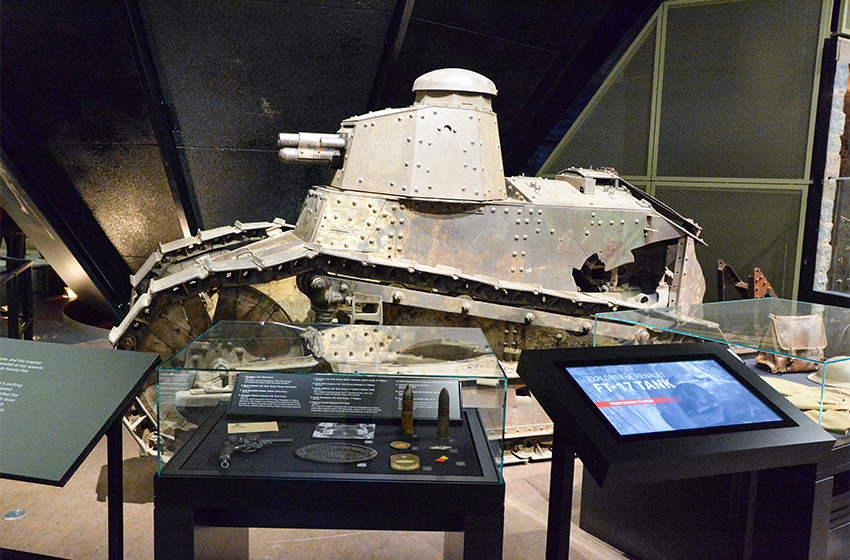 Modern photograph of the tank exhibit from another angle. Between the viewer and the tank are a static informational display and an interactive screen display.