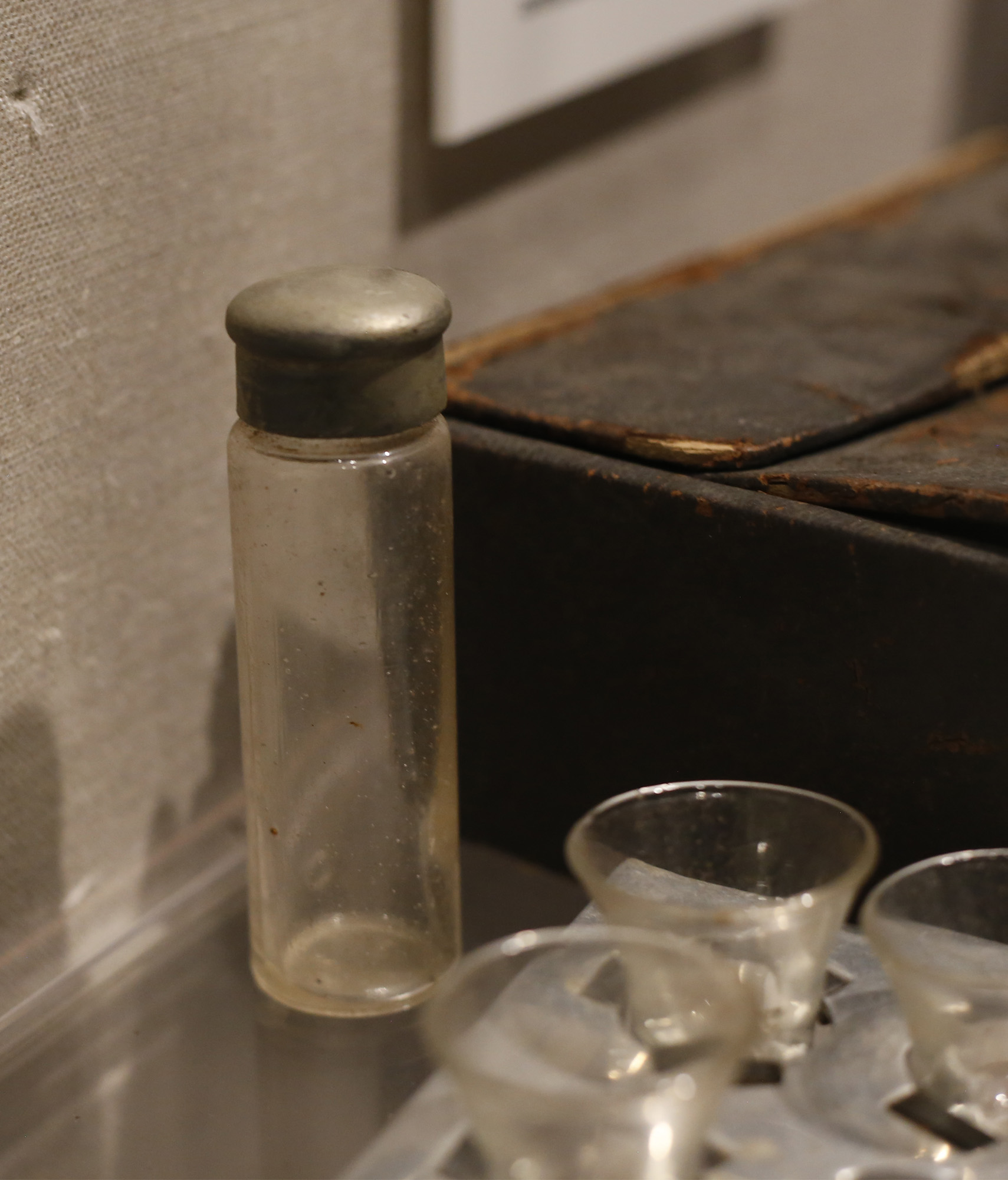 Photographie moderne d'un petit flacon en verre avec un bouchon en métal émoussé situé dans une vitrine de musée