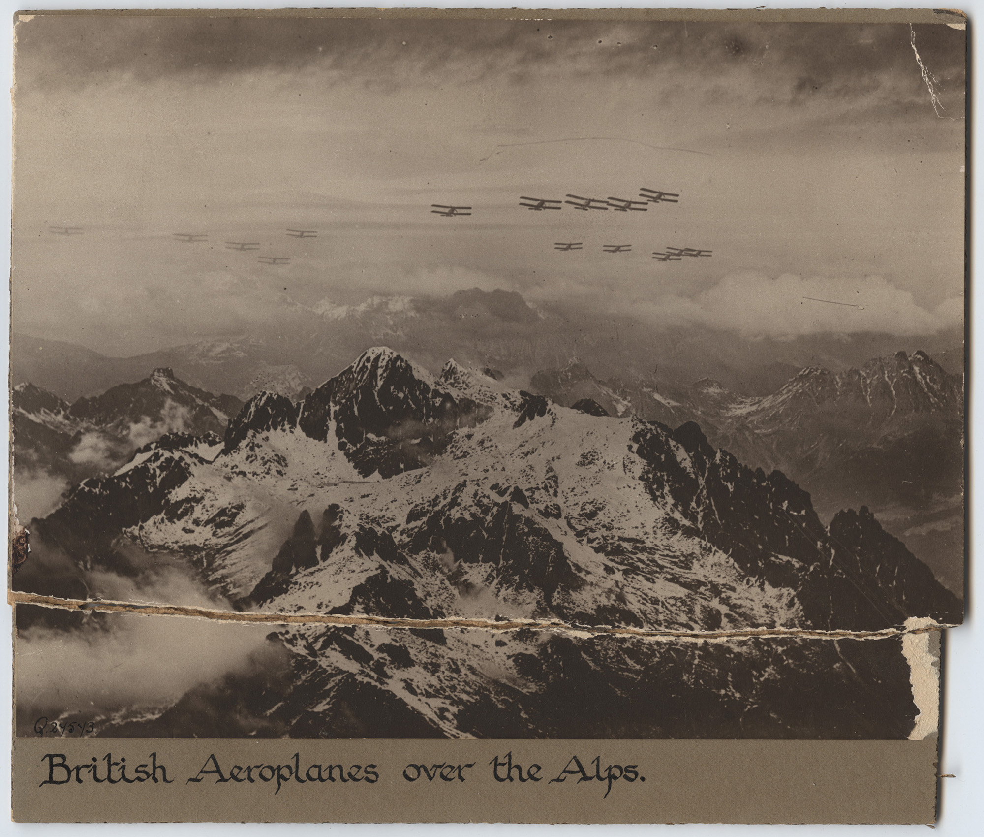 Black and white aerial photograph of a snowy mountain range with WWI aircraft flying over the peaks