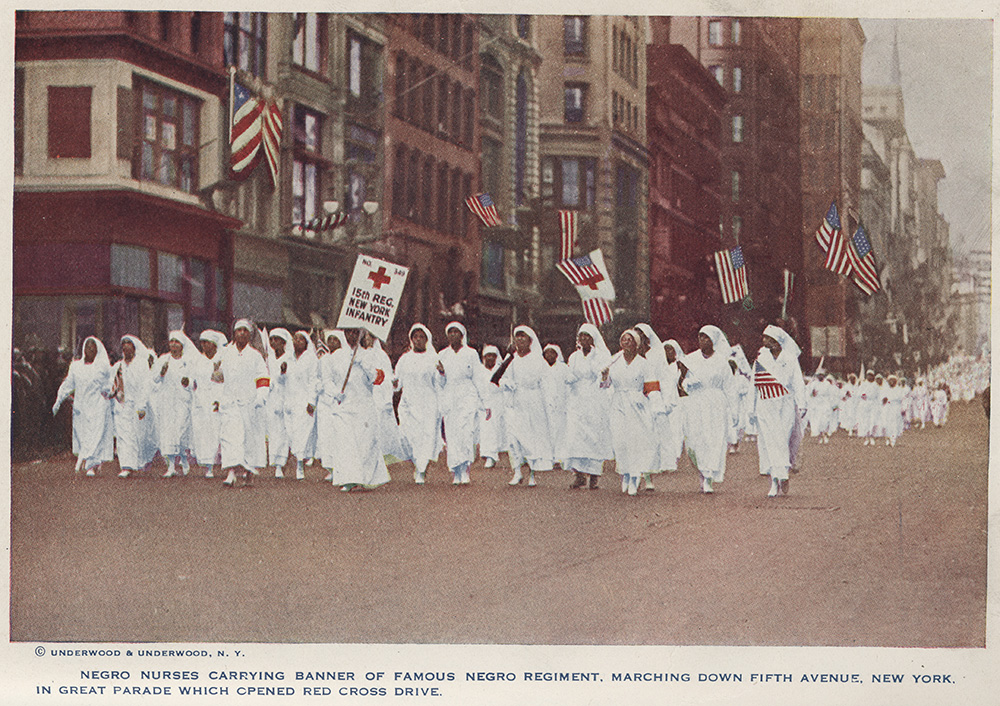 Colorized photograph of a large group of Black women nurses dressed in white uniforms marching down a city street