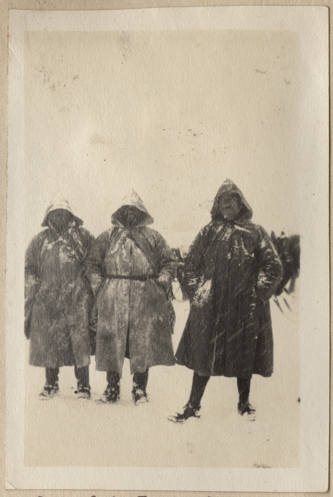 Black and white photograph of three men in heavy coats and hoods standing in the snow