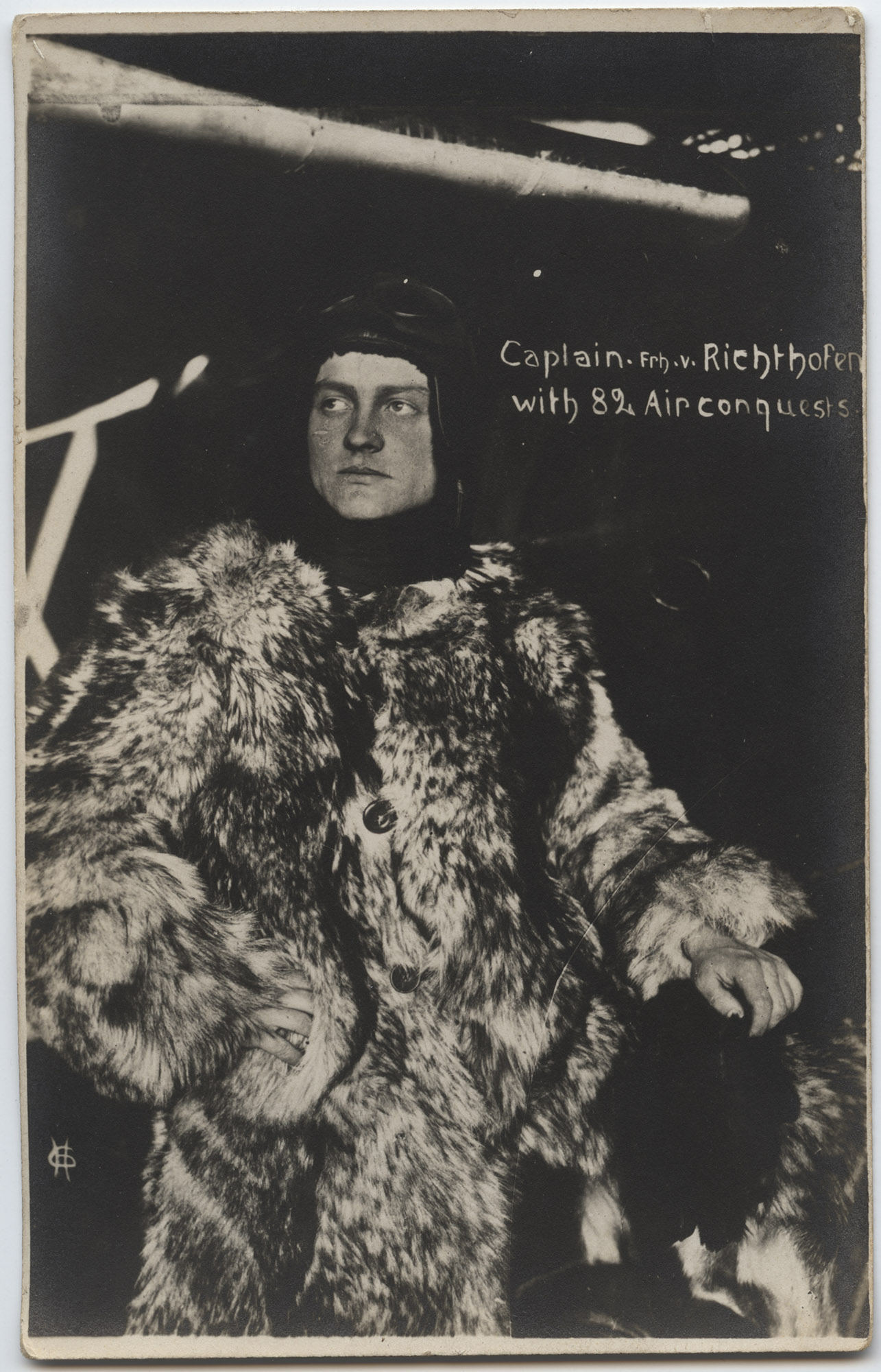 Black and white portrait photograph of a young white man posing in a large fur coat and leather aviator cap