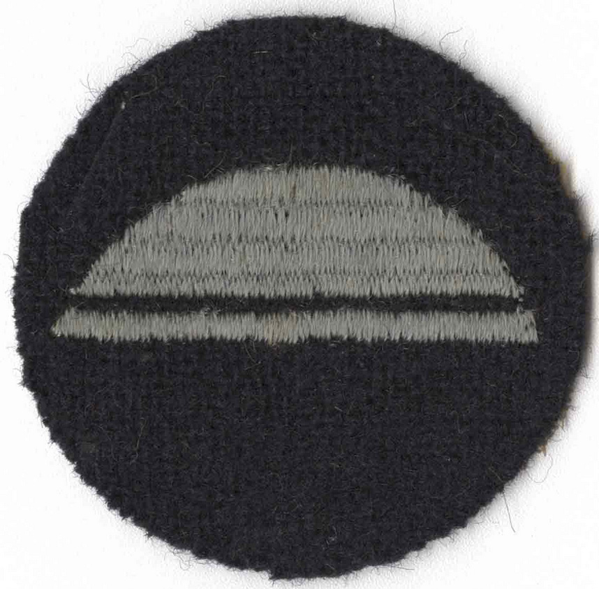 Circular black insignia patch embroidered with a blue helmet